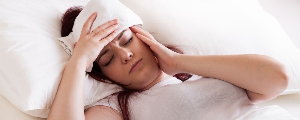 Vrouw die met hoofdpijn aan de linkerkant op bed ligt