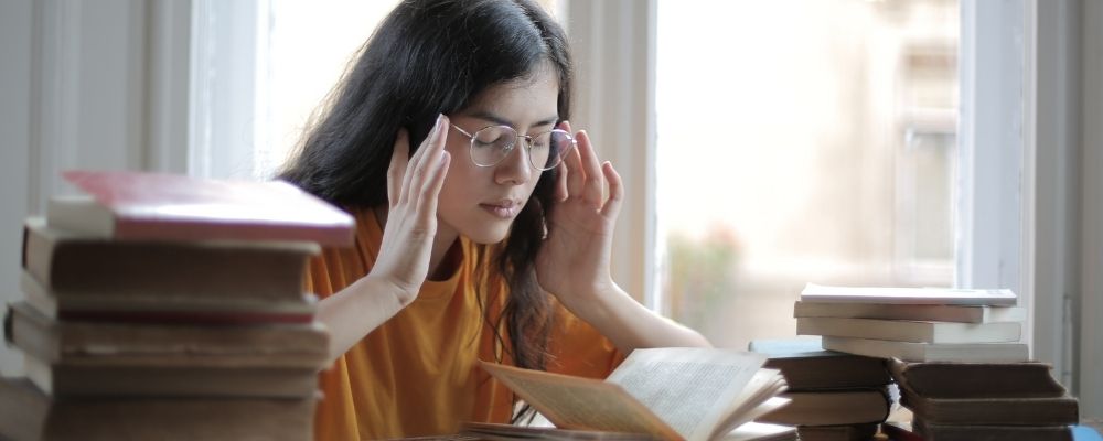 Woman rests fingers on her temples while trying to read a book and suffers from indecision