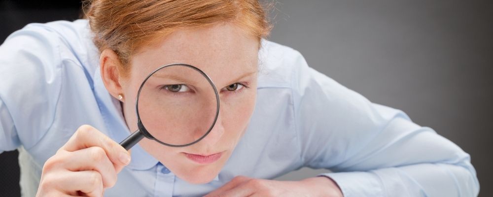 Woman looking through a magnifying glass towards the camera