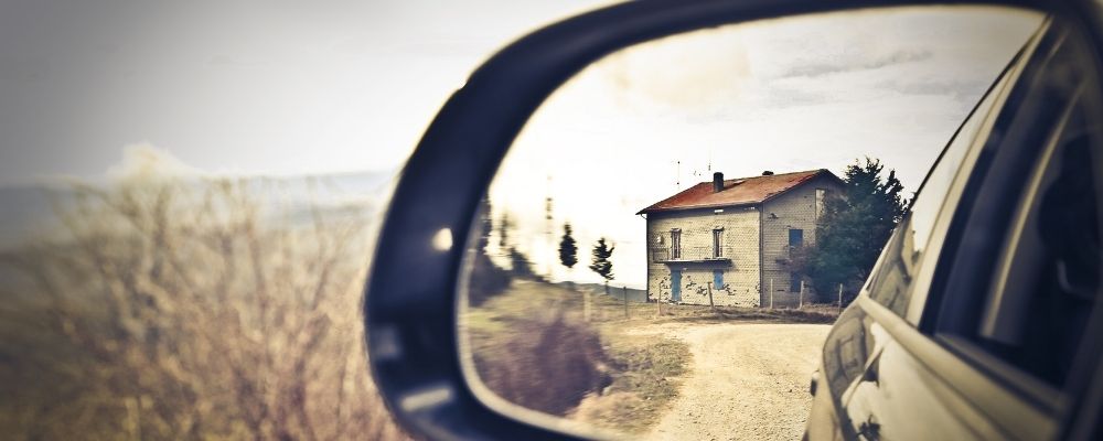 Mensen rijden weg in een auto en zien hun huis in de achteruitkijkspiegel