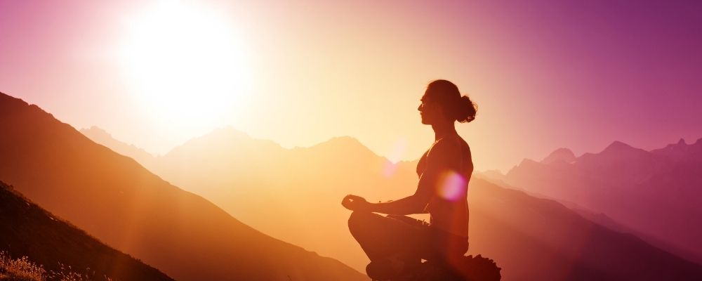 Vrouw mediteert bij een ondergaande zon