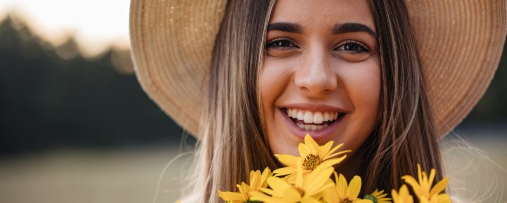 Vrouw met hoed op en bloemen in haar hand lacht
