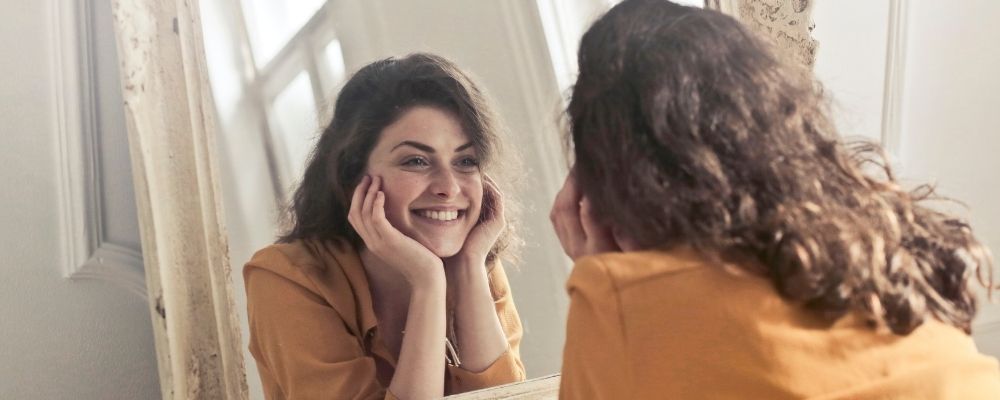 Vrouw kijkt lachend in de spiegel door positieve affirmaties