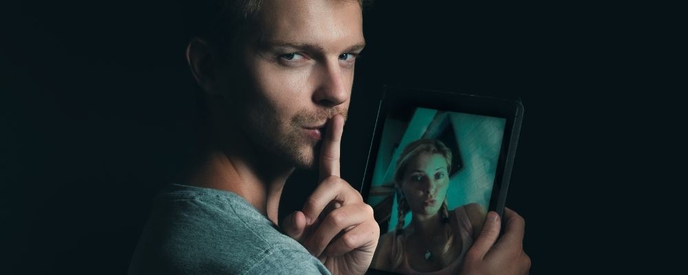 Man kijkt om met zijn vinger tegen zijn mond en met een meisje op zijn tablet