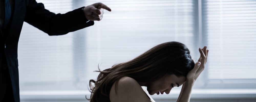 Vrouw die beschuldigd wordt door een man terwijl ze haar handen tegen haar voorhoofd houdt en naar beneden kijkt
