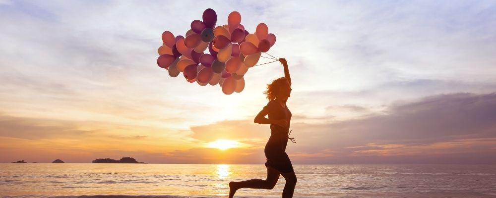 Vrouw die met veel ballonen in haar hand over het strand rent