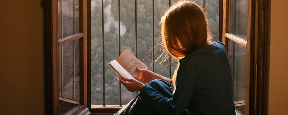 Introverte vrouw die een boek aan het lezen is bij het raam