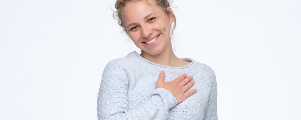 Vrouw die haar hand tegen haar borst houdt en breed lacht
