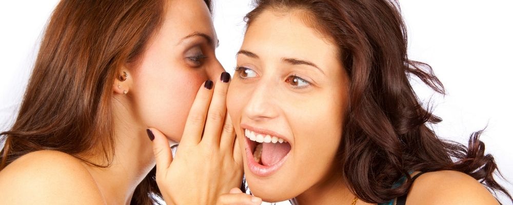 Vrouw praat in het oor van een andere vrouw die verbaasd kijkt