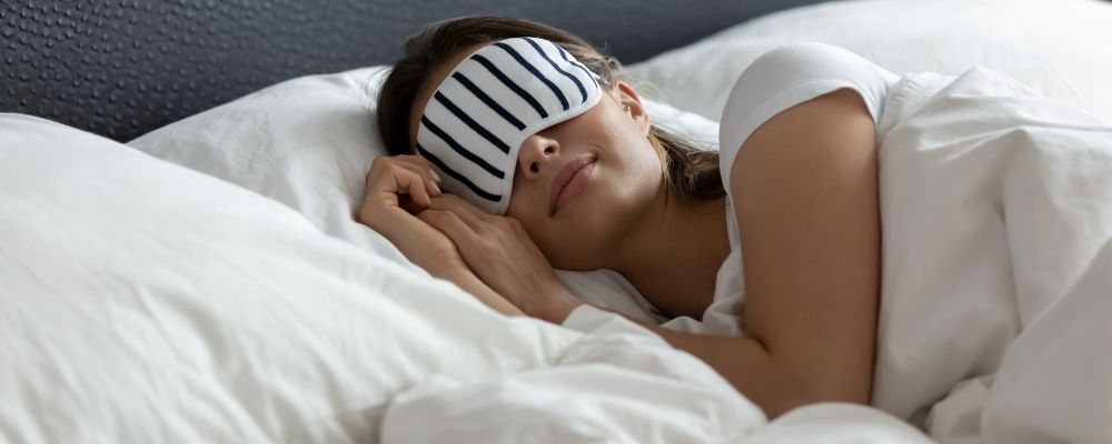 Vrouw die in bed ligt met een nachtmasker op