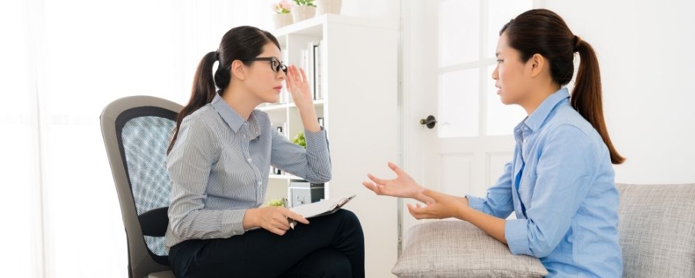 Vrouw die met een therapeute praat die haar bril vasthoudt en in shock kijkt