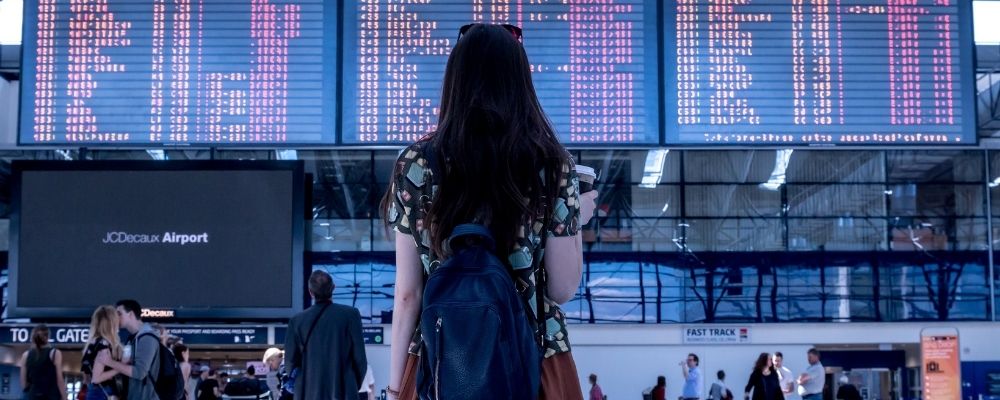 Vrouw die met een koffer die naar de vluchten kijkt op een vliegveld