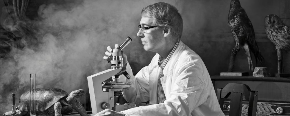 Zwart wit foto van een wetenschapper die in een microscoop kijkt