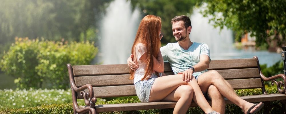 Man en vrouw die samen op een bankje zitten in de natuur terwijl de man zijn hand op de knie van de vrouw heeft