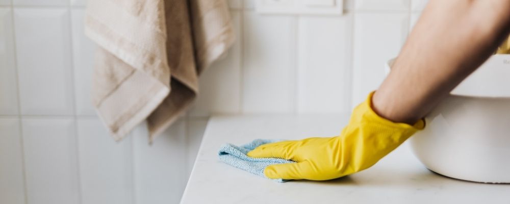 Persoon die met een gele handschoen de wastafel aan het schoonmaken is