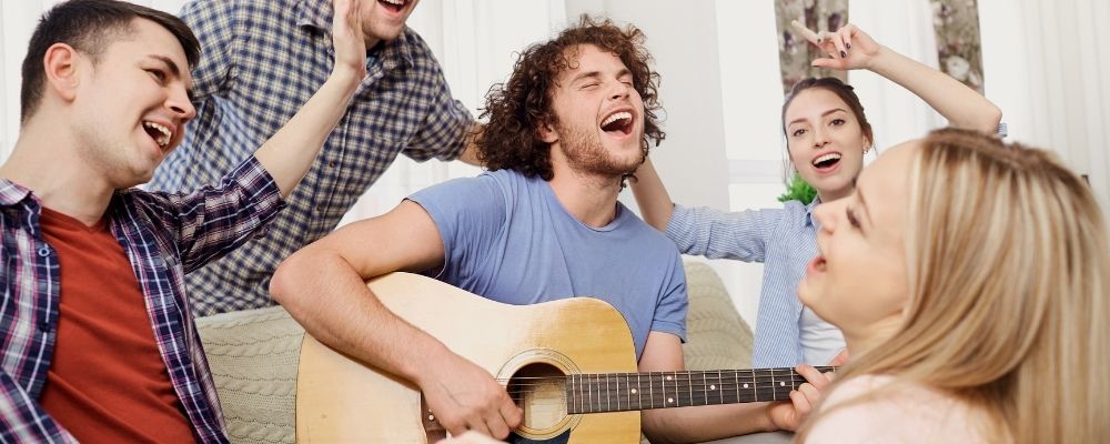 Man die gitaar speelt en vrienden om hem heen lachen