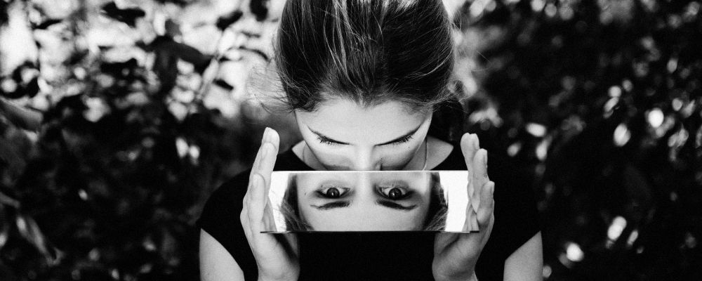Vrouw die een spiegel vasthoudt en via de spiegel naar de camera kijkt
