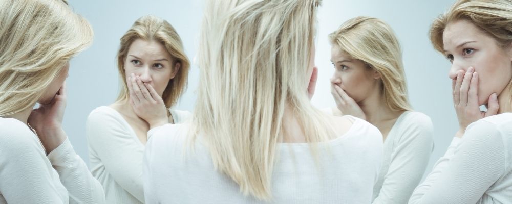 Vrouw die vragend naar vier spiegelbeelden van zichzelf kijkt