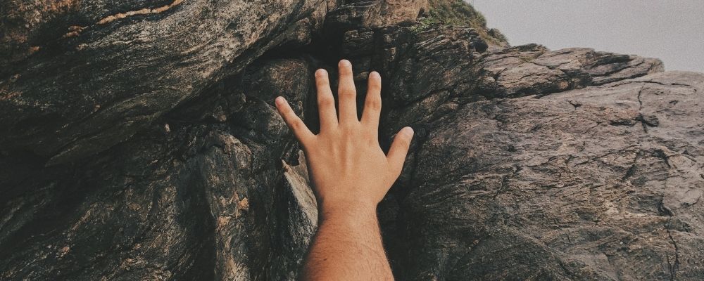 Hand die naar boven rijkt om een rots te beklimmen