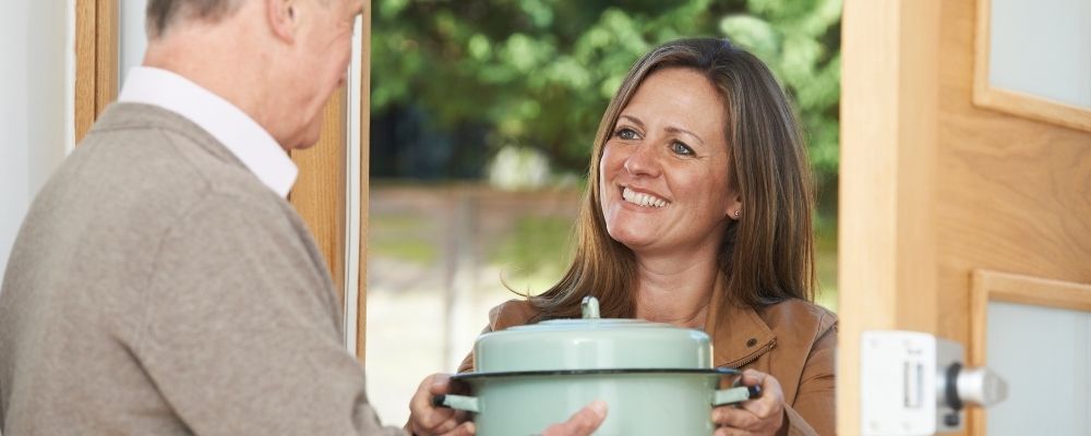 Vrouw die een pan met eten geeft aan haar buurman