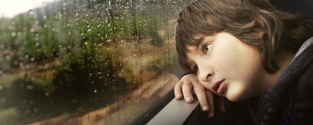Kind dat eenzaam uit het raam kijkt waar regendruppels opvallen