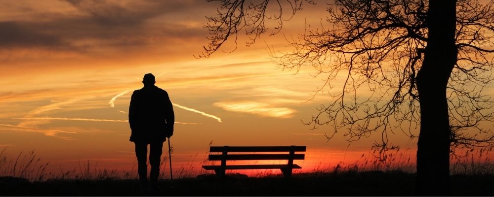 Eenzame man die naast een bankje staat en naar de natuur kijkt