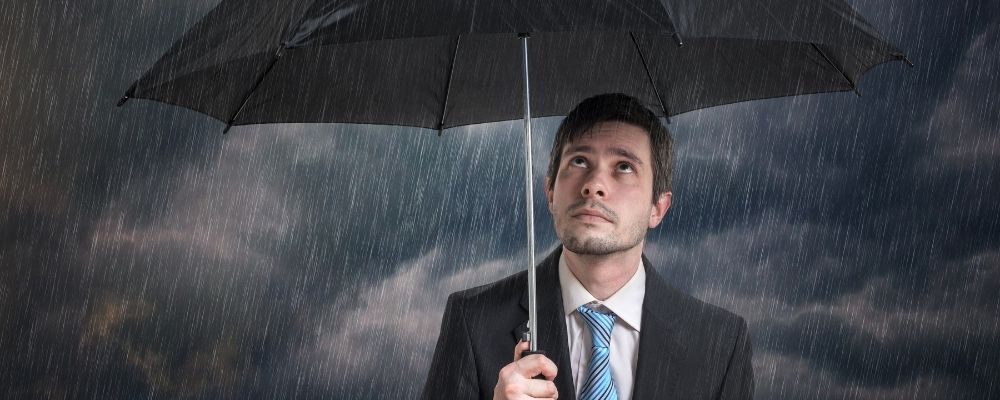 Man die bedroefd omhoog kijkt naar de regen terwijl hij een paraplu vasthoudt