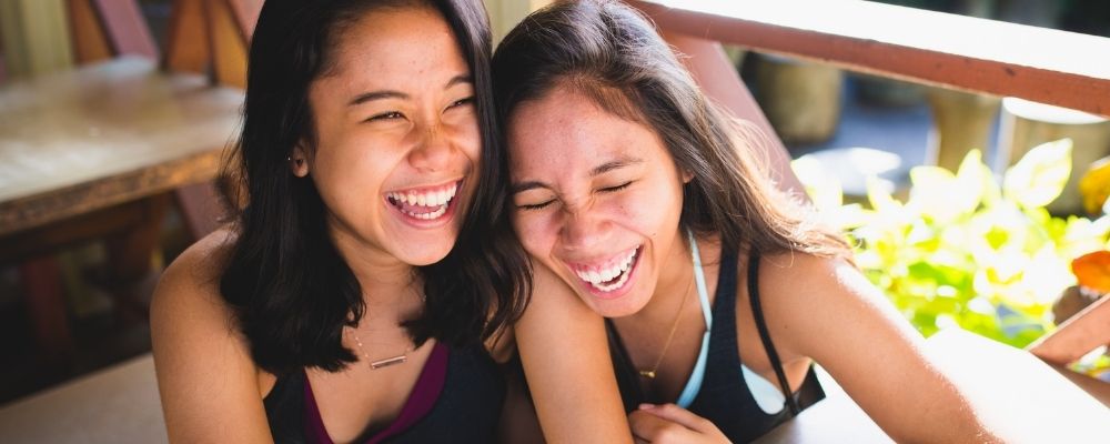 Twee meiden die samen hard aan het lachen zijn en waarbij de ene op de schouder van de andere leunt