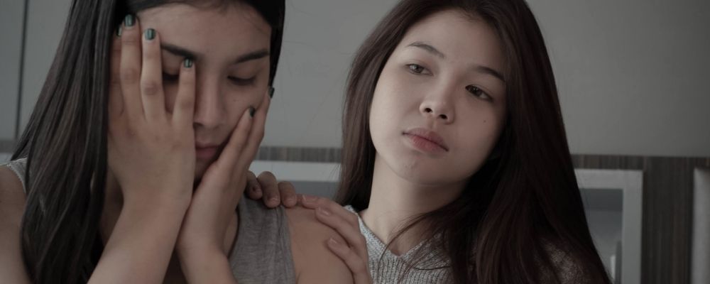 Vrouw die haar handen in haar gezicht houdt en haar vriendin probeert haar te kalmeren