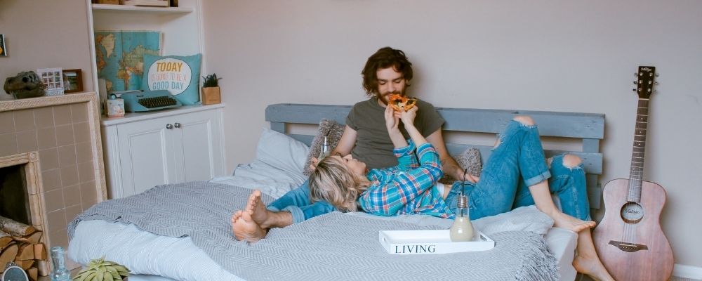 Man en vrouw die samen op bed liggen en pizza eten